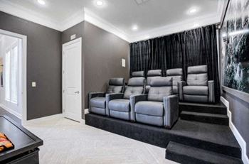 A home theater with a row of grey leather seats and a black carpet.